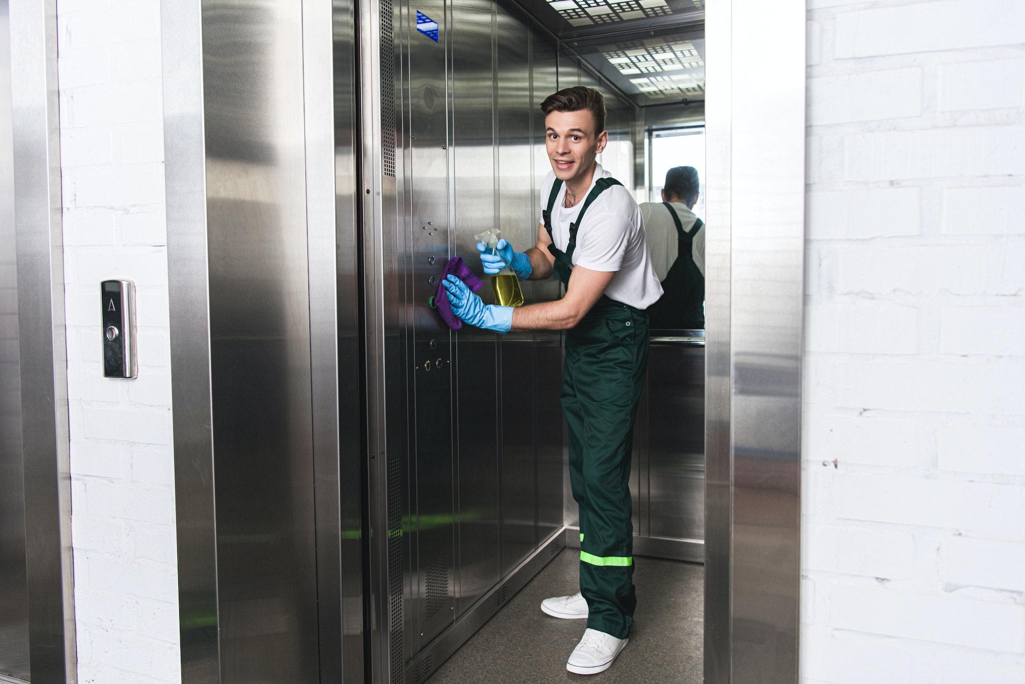 handsome young man cleaning elevator and smiling at camera